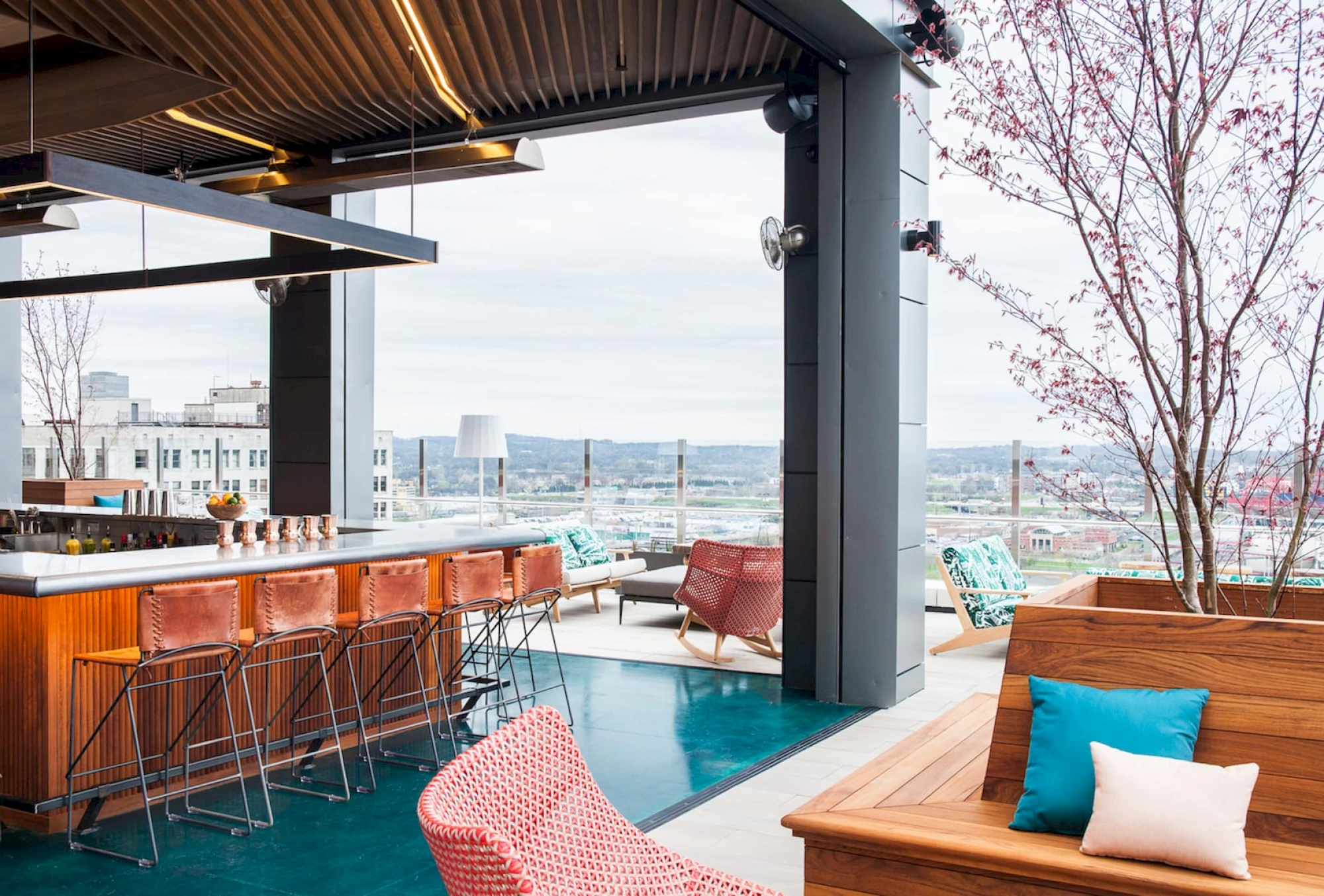 A rooftop bar with a counter, barstools, and lounge seating area with a city view.