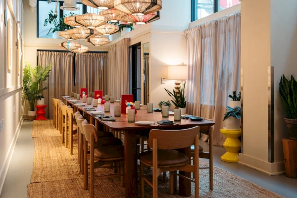 A long dining table set with chairs and decorations in a room with high ceilings and large windows.