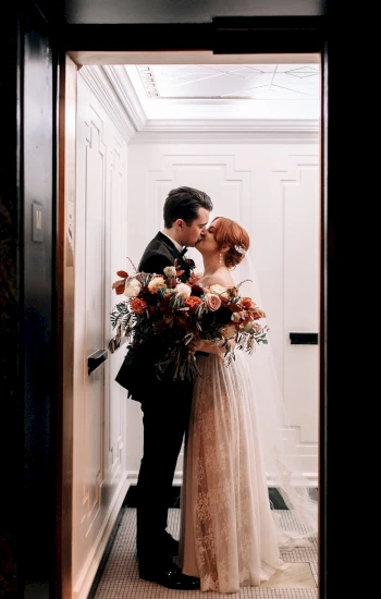 A couple in wedding attire kissing in a hallway.