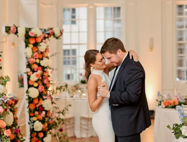 A couple dancing in a decorated room with flowers and tables.
