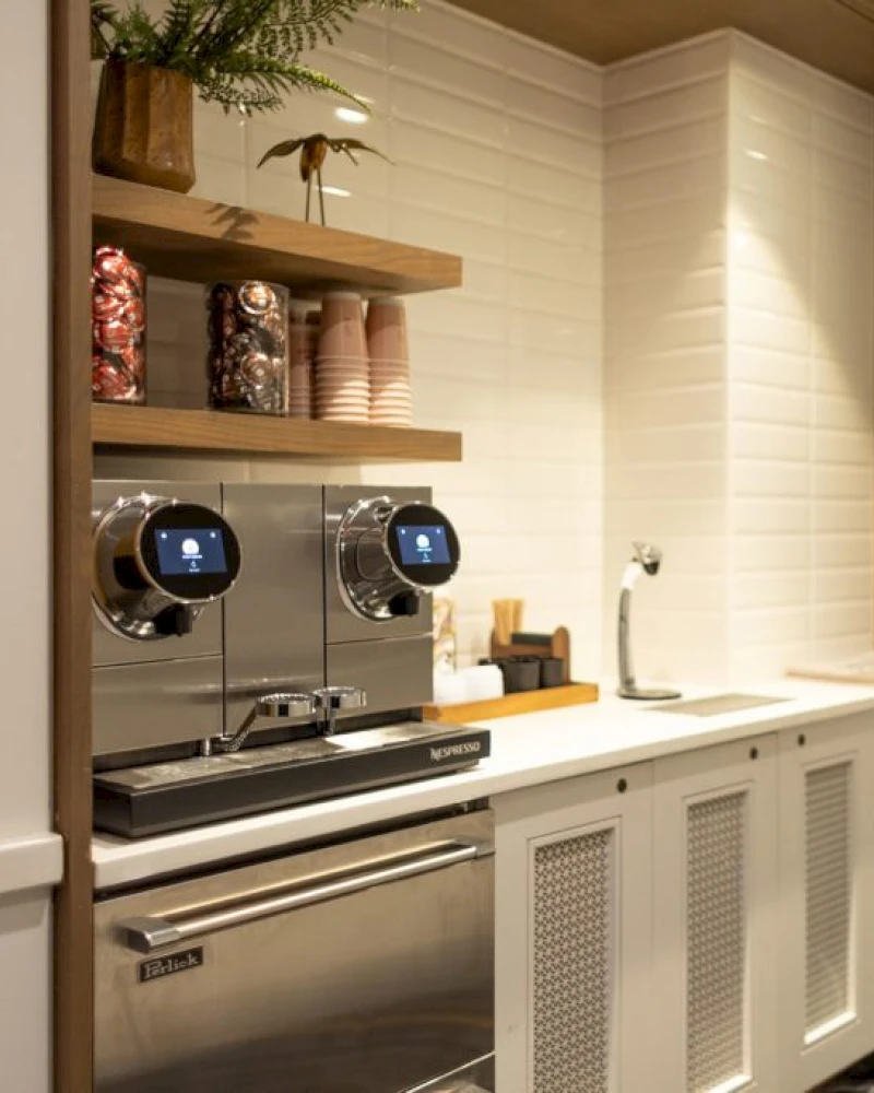 A kitchenette with a coffee maker, stainless steel appliances, and white cabinets.