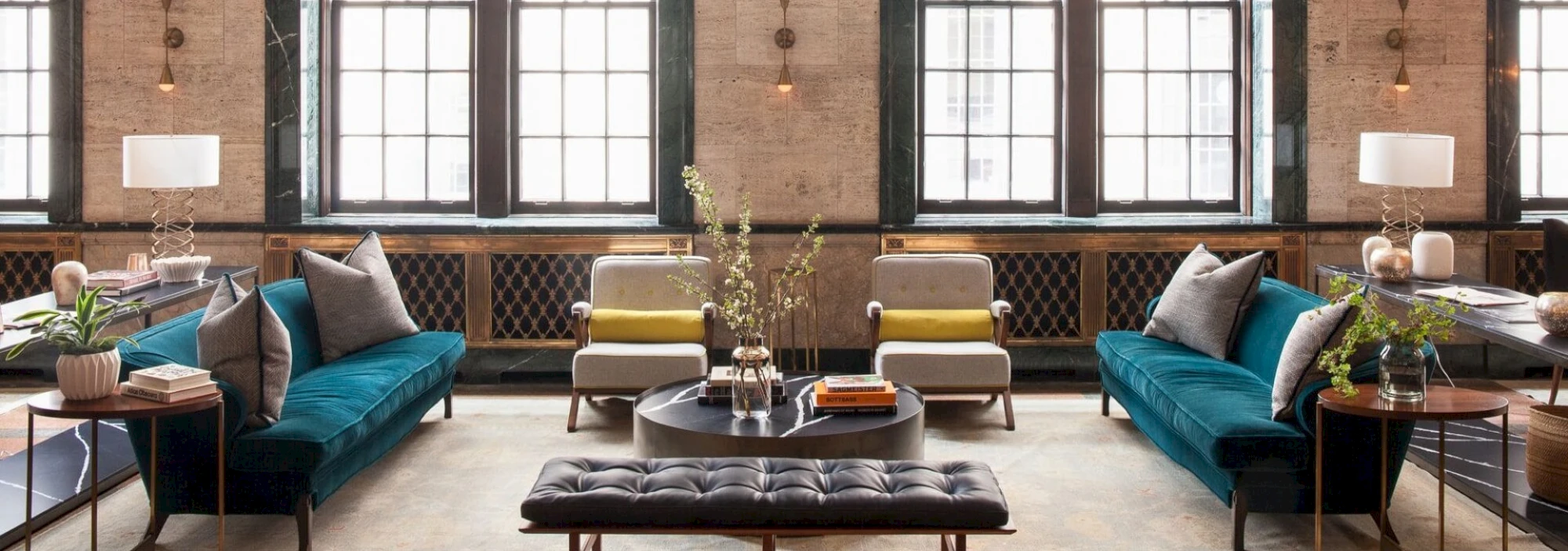 A stylish lobby with a teal sofa, coffee table, armchairs, and lamps.