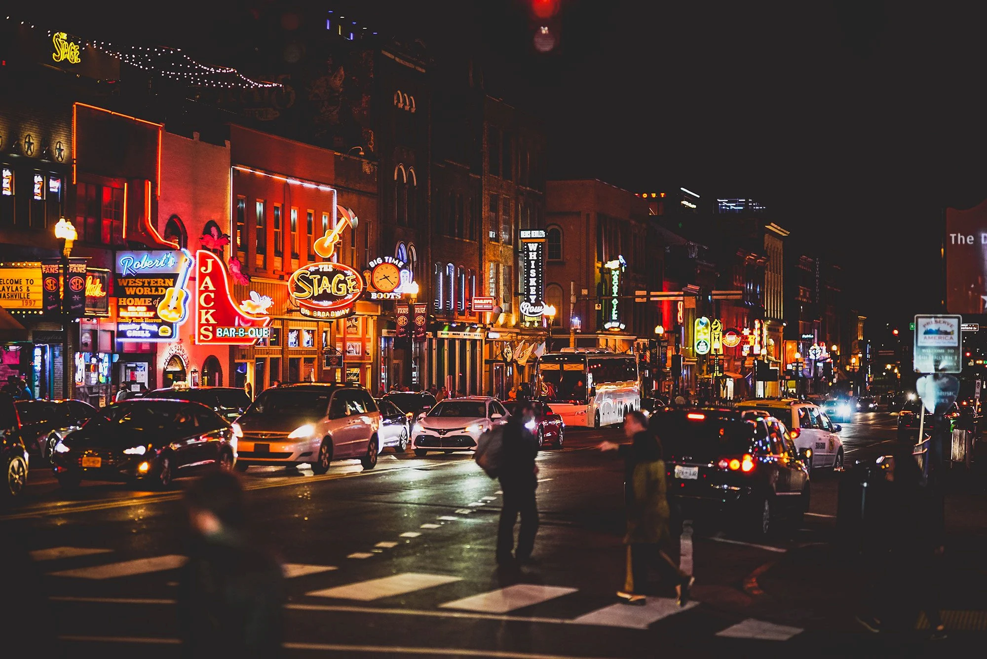 A nighttime view of a lively city street with neon signs, cars, and people.
