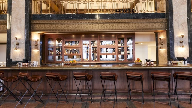 A wide view of a bar with a long counter, several stools, and a decorative backlit shelf with bottles.