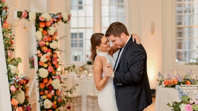 A couple dancing in a decorated event space with flowers and tables.