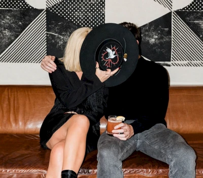 A couple sitting on a brown leather sofa in a bar, with a black and white wall in the background.