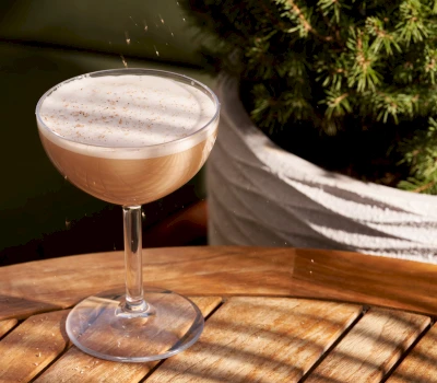 A cocktail on a wooden table with a potted plant in the background.