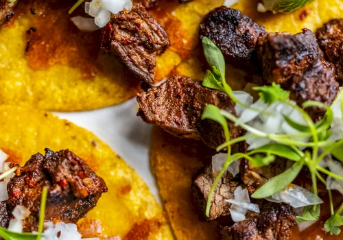A close-up of tacos with meat, onion, and greens.