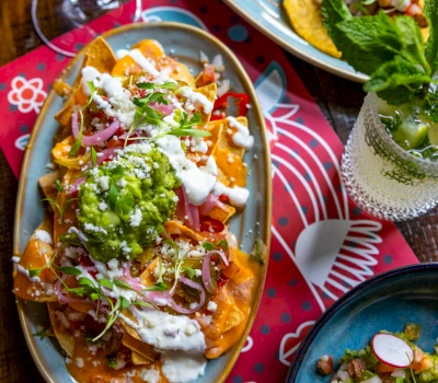 A plate of nachos with toppings and a drink on a table.