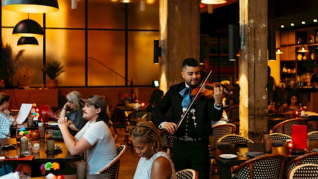 A lively restaurant with diners at tables and a musician playing the violin, all set in a warm, inviting atmosphere.