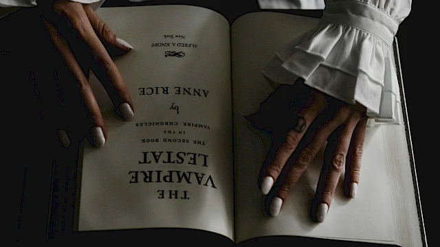 A person with elegant, ruffled sleeves holds open a book titled 