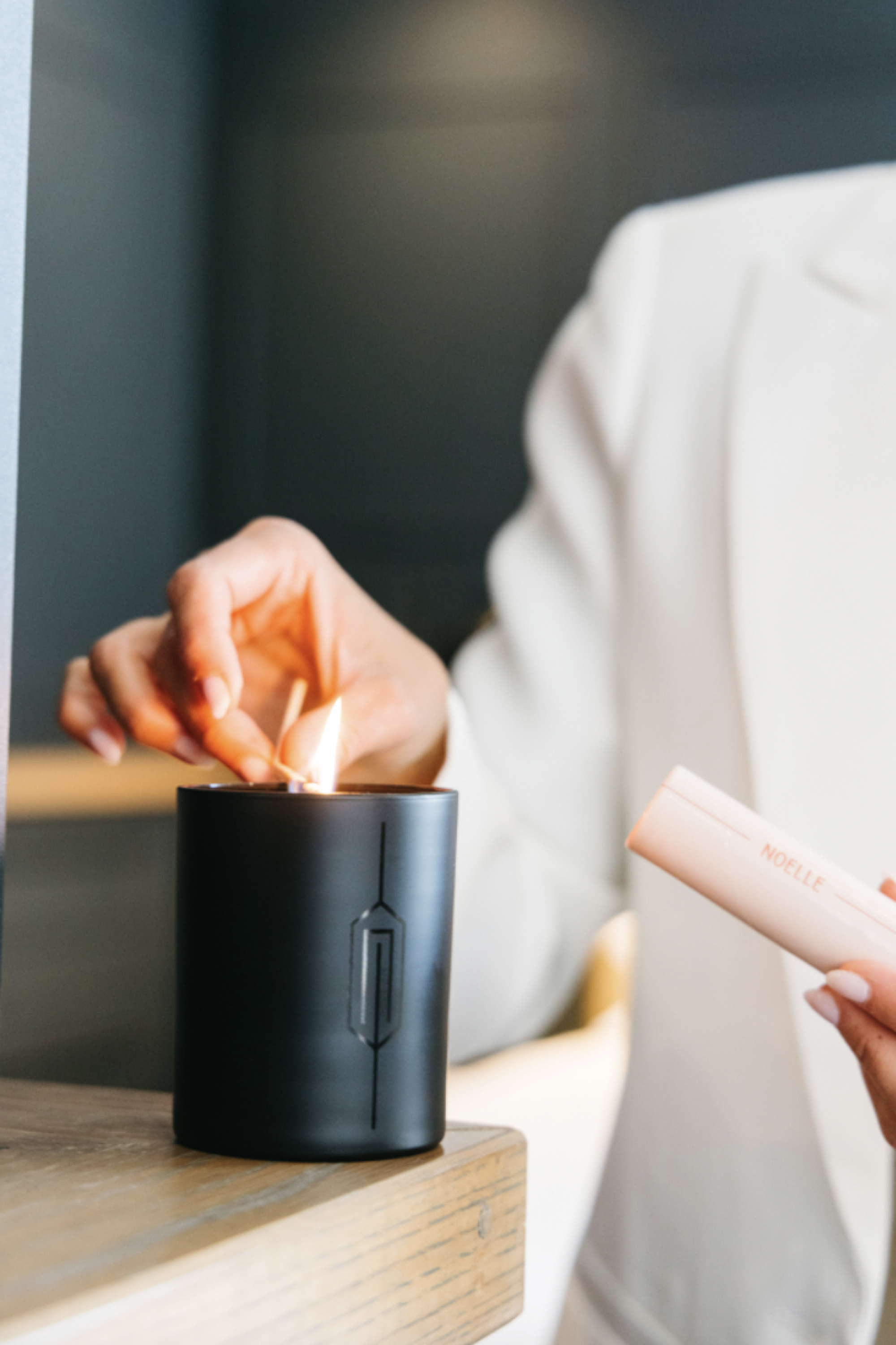 A person lighting a black candle with a small device, wearing a white outfit, on a wooden surface.
