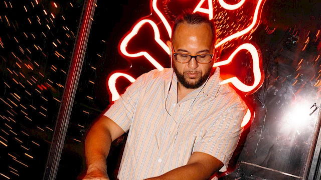 A DJ is playing music with a neon skull and crossbones in the background, surrounded by Halloween-themed decorations.