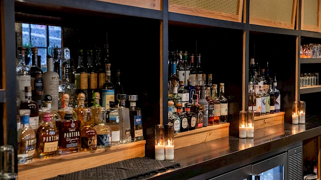 A bar shelf with various liquor bottles and lit candles.