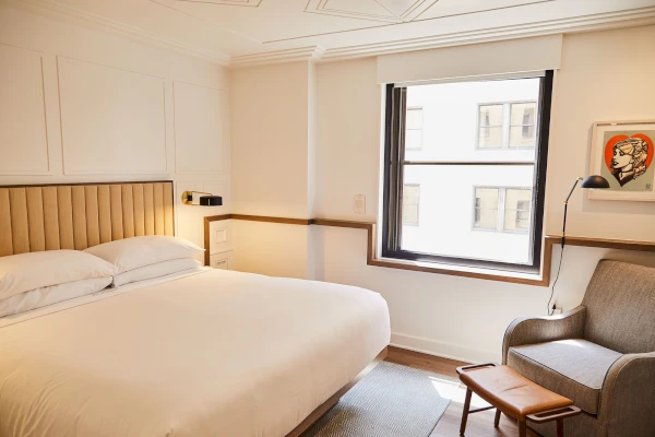 A bright and airy hotel room with a large bed, comfortable chair, and a window with a city view.