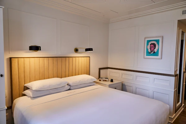 A hotel room with a large bed, wooden headboard, and white linens.