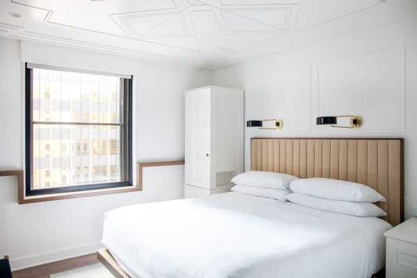 A white bedroom with a large bed, wooden headboard, and a window