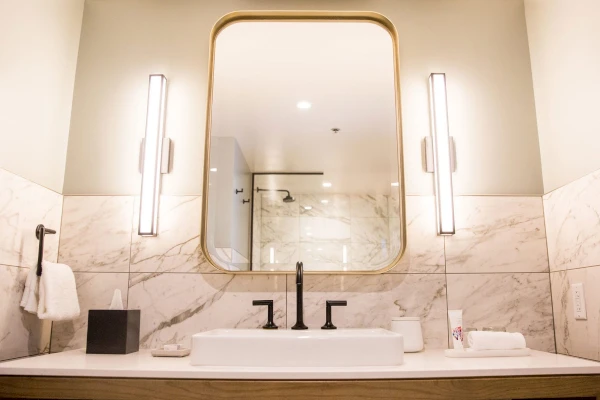 A bathroom sink area with a large mirror, marble tile, and modern fixtures.