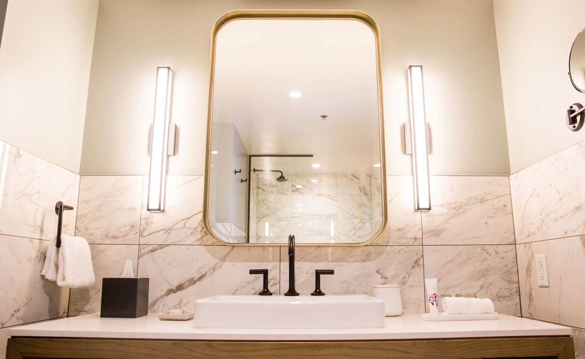 A bathroom sink area with a large mirror, marble tiles, and modern fixtures.