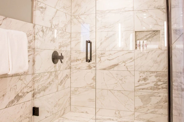 A marble-tiled shower with a glass door, a towel on the wall, and a shower head with a handle.
