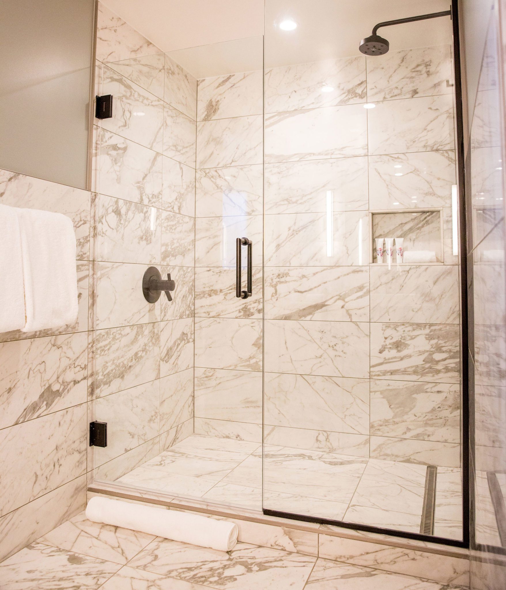 A marble-tiled shower with a glass door and a rain showerhead