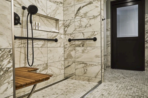 A marble-tiled shower with a wooden bench, grab bars, and a rain showerhead.