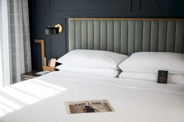 A close-up of a neatly made bed with white bedding and pillows, a gray upholstered headboard, and a nightstand with a magazine on it.