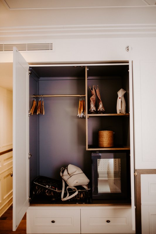 A closet with open doors showing a hanging rod, shelves with accessories, and a mini-fridge.