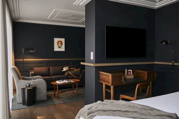 A wide view of a hotel room with a desk, TV, sofa, bed, and chair.