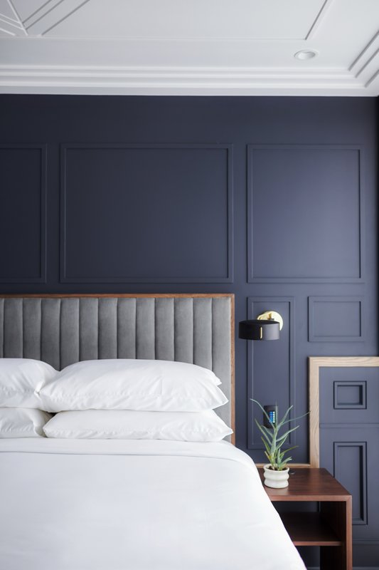 A bed with white linens and pillows against a dark blue wall with molding.