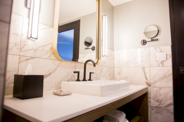 A bathroom sink with a white countertop, black faucet, and marble tile walls.