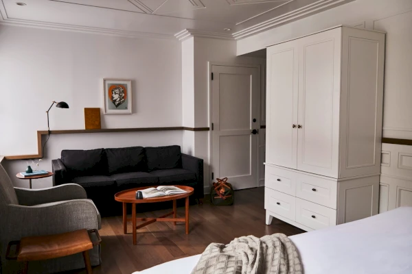 A wide view of a hotel room with a sofa, coffee table, armchair, and wardrobe.