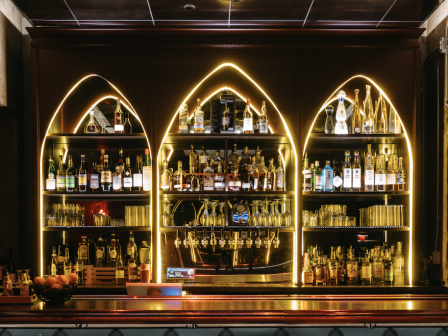 A backlit bar with shelves of various liquor bottles and glasses.