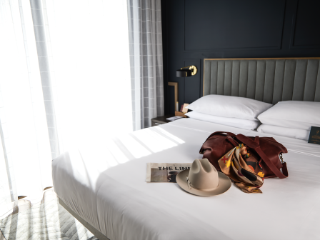 A bed with a hat, newspaper, and bag in a sunny room.