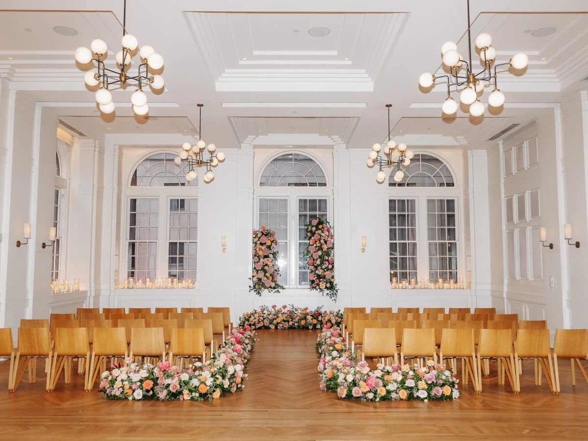a large room with white walls, wooden chairs, and floral decorations