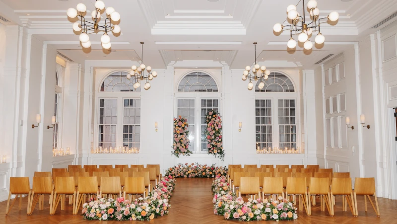 A brightly lit room with white walls, large windows, and a floral arrangement set up for an event.