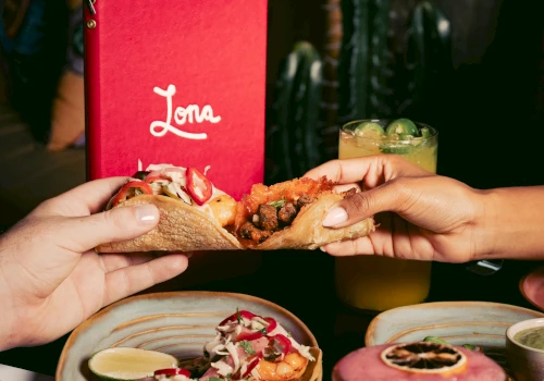 A hand holding a taco with a red menu in the background